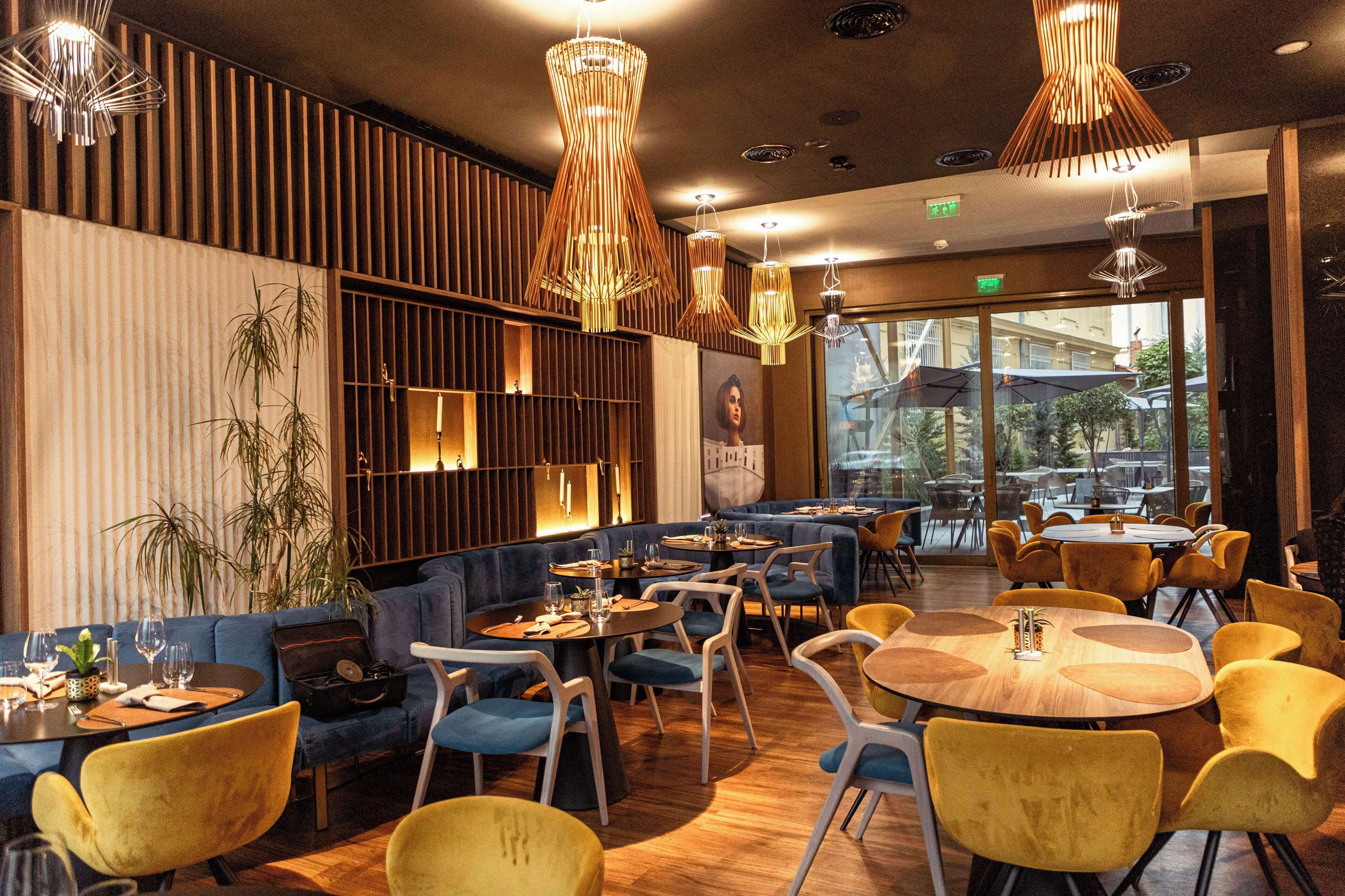 Ein Restaurantinneres mit runden Tischen, gelben Stühlen und blauen Sofas.
