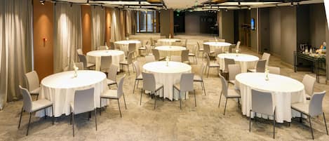 A hotel conference room with multiple round tables and chairs, carpeted flooring, and curtains along the walls.