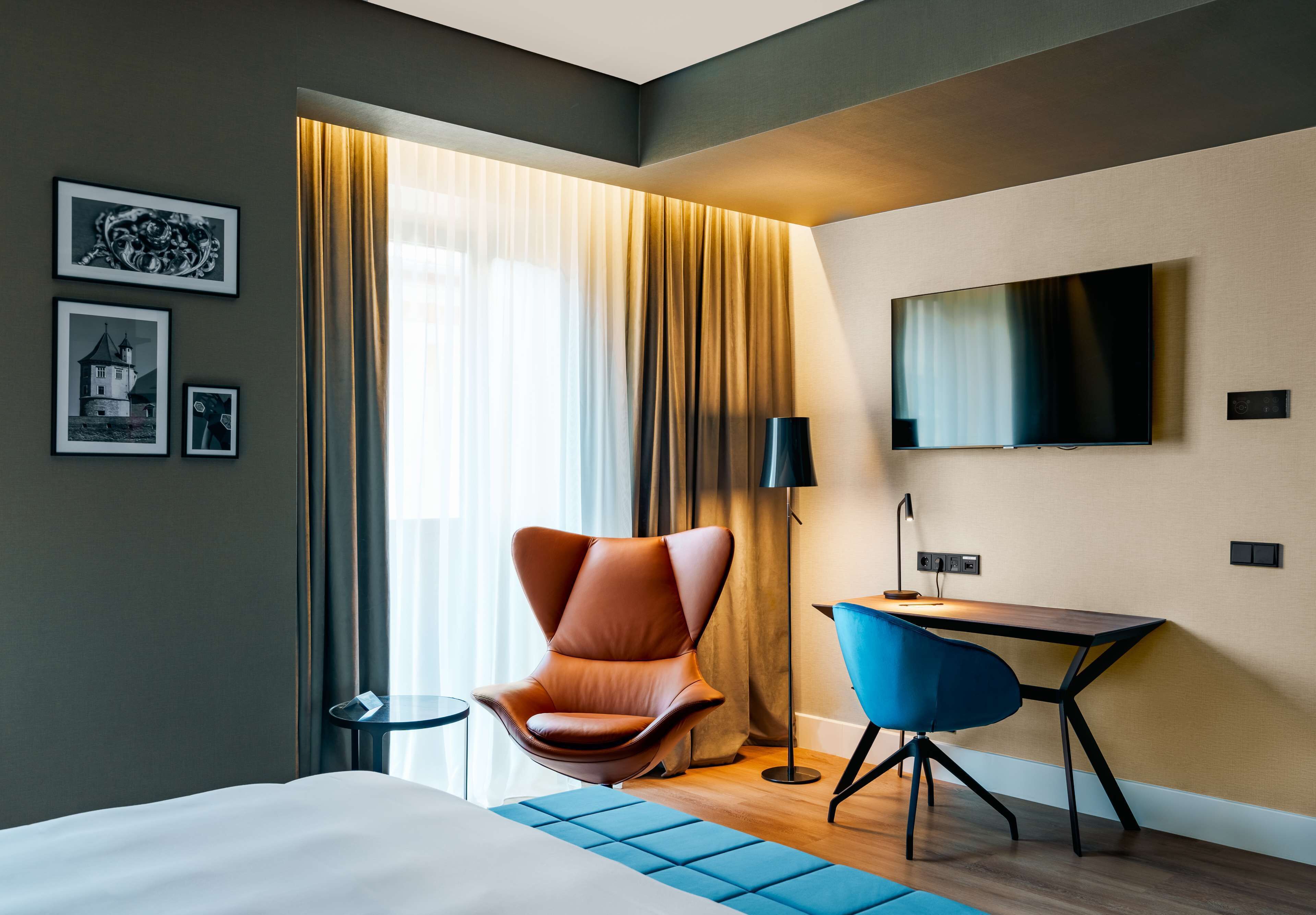 A modern hotel room with a large bed, a desk, a chair, and a TV mounted on the wall.