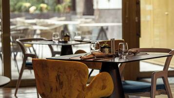 A restaurant interior with a modern design, featuring a mix of wooden and metal furniture, a glass dining area, and a view of the outdoor seating area.