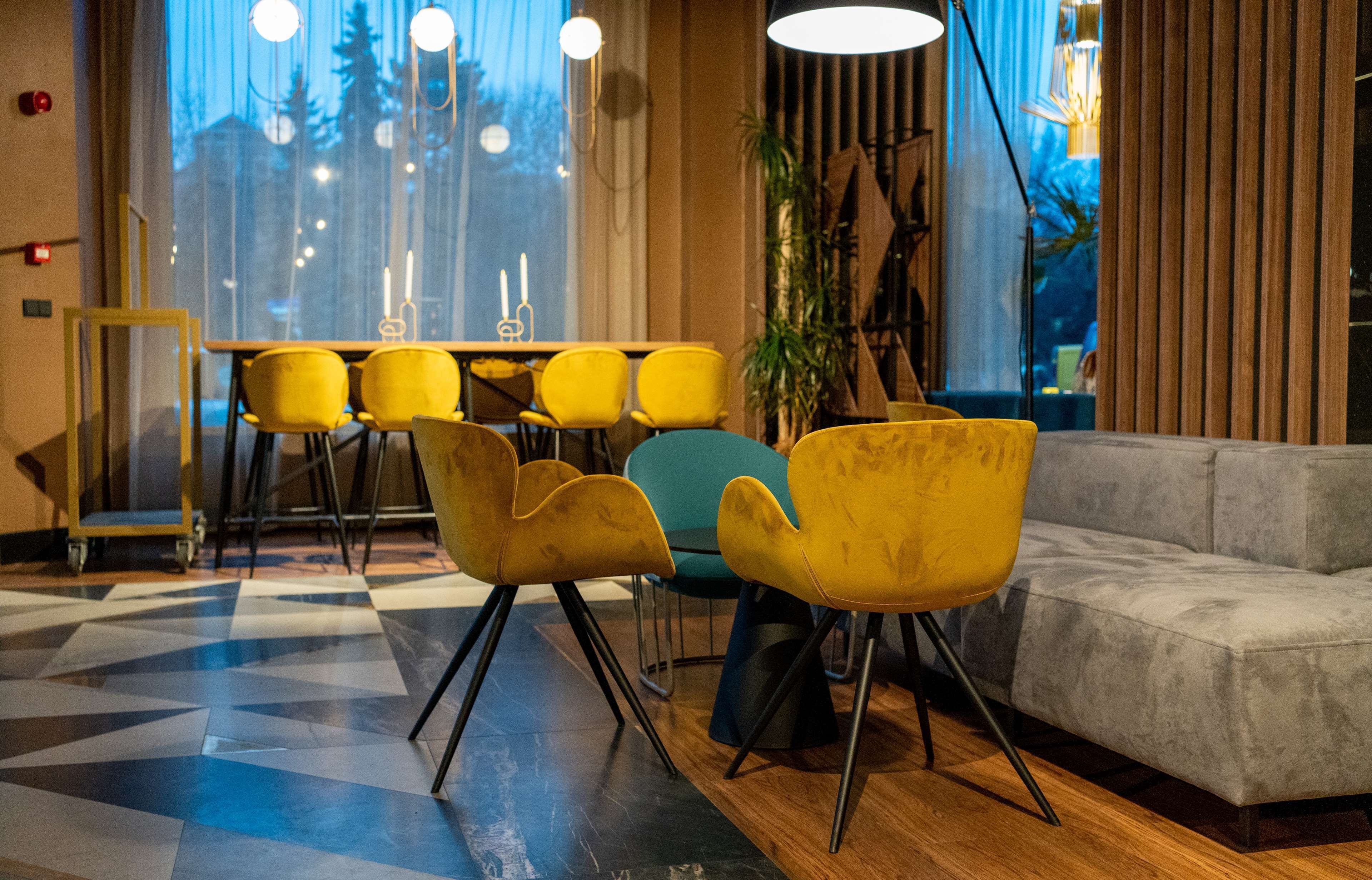 A modern interior with a dining area featuring yellow chairs, a grey sofa, and a patterned floor.