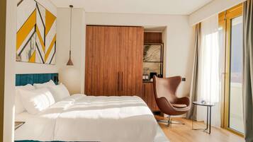 A modern hotel room with a large bed, a wooden wardrobe, a brown chair, and a view of the outdoors.