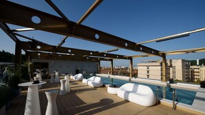 A rooftop pool area with white seating and a clear view of the city skyline.