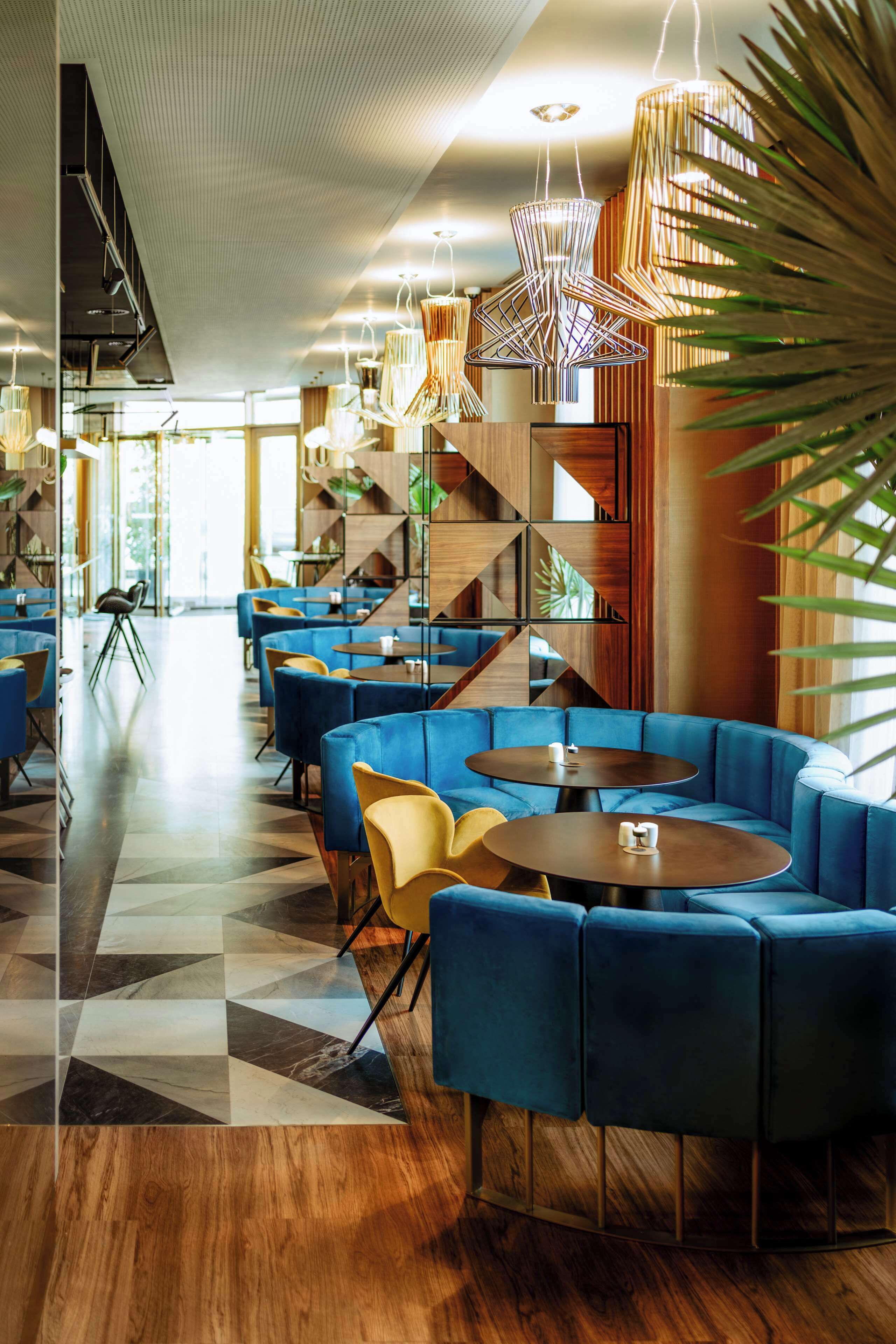A modern lounge area with blue seating, wooden flooring, and geometric wall designs.