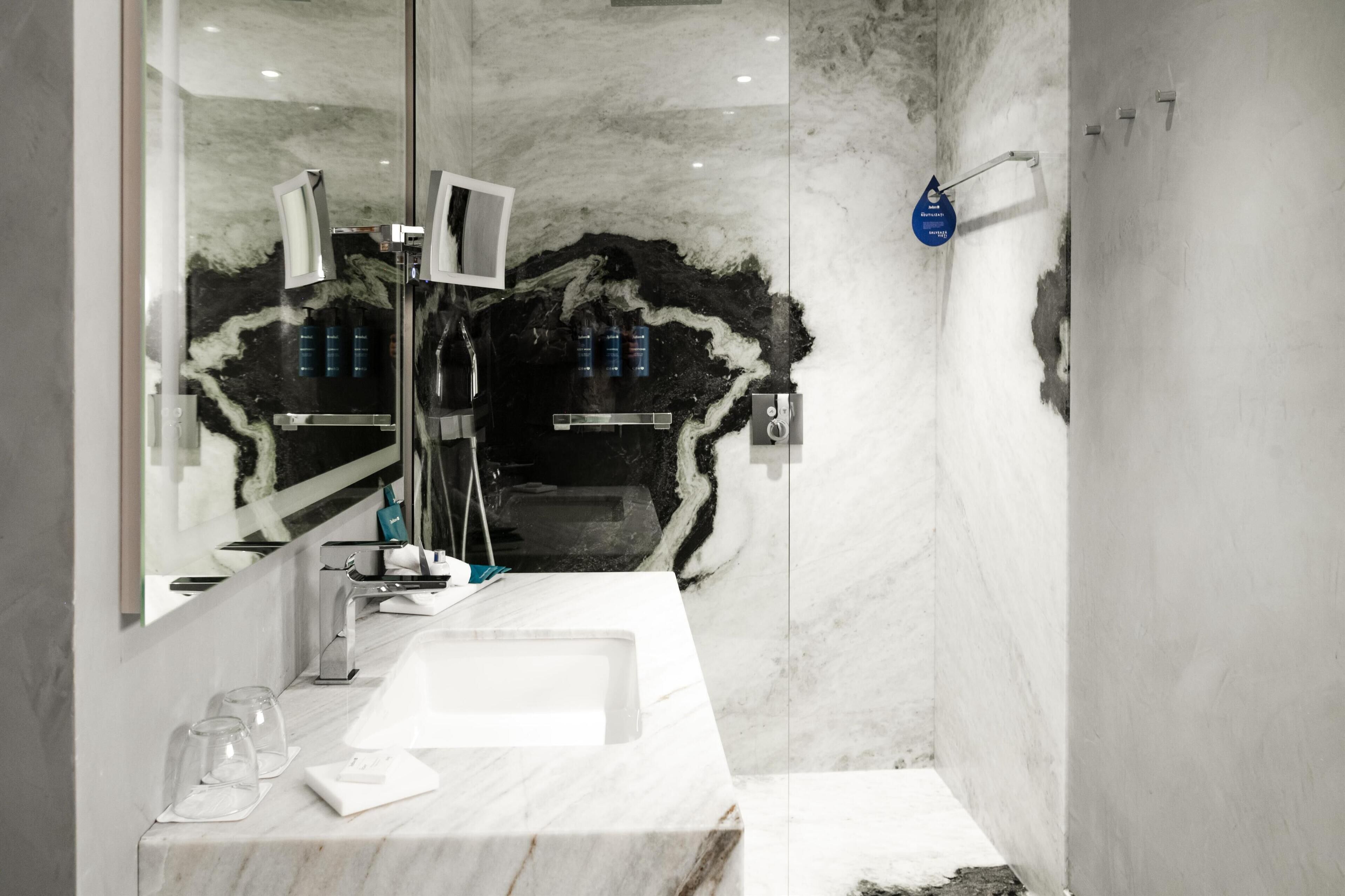 Un bagno moderno con un mobile vanitario in marmo, uno specchio grande e uno spazio doccia.