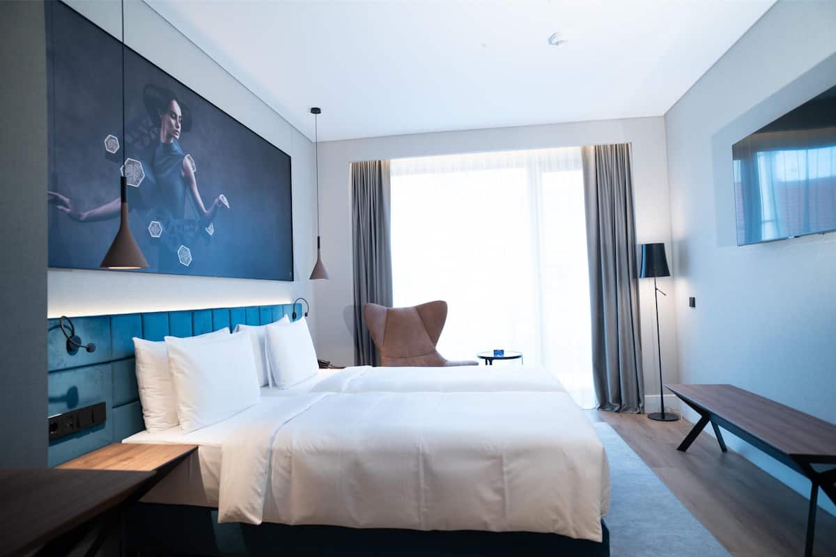 A modern hotel room with a large bed, a desk, a chair, and a TV mounted on the wall.