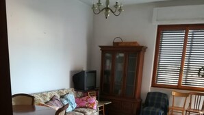 A living room with a sofa, a television, a cabinet, and a dining table. - Central Apartment (margherita di savoia)