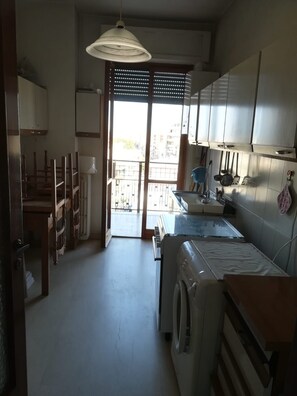 A compact kitchen with a washing machine, a sink, and a dining area with chairs. - Central Apartment (margherita di savoia)