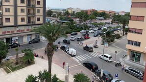 A multi-story building with balconies, a busy street with cars and pedestrians, and palm trees. - Central Apartment (margherita di savoia)