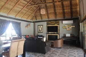 Uma sala de estar com telhado de palha, um sofá, uma televisão e uma mesa com uma guitarra.