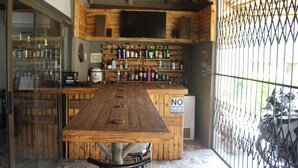 Una zona de bar con una mesa de madera, estantes llenos de botellas y un televisor montado en la pared.