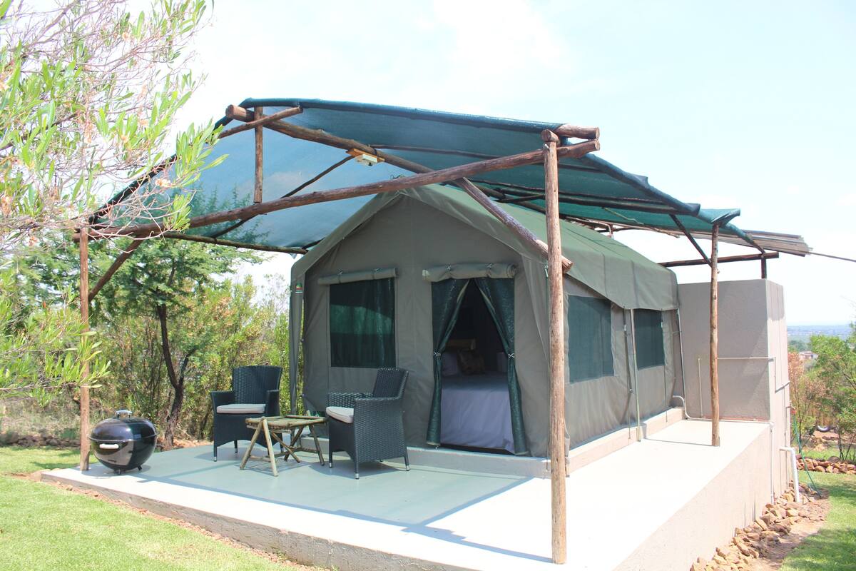 A tent with a covered patio area, a grill, and two chairs.