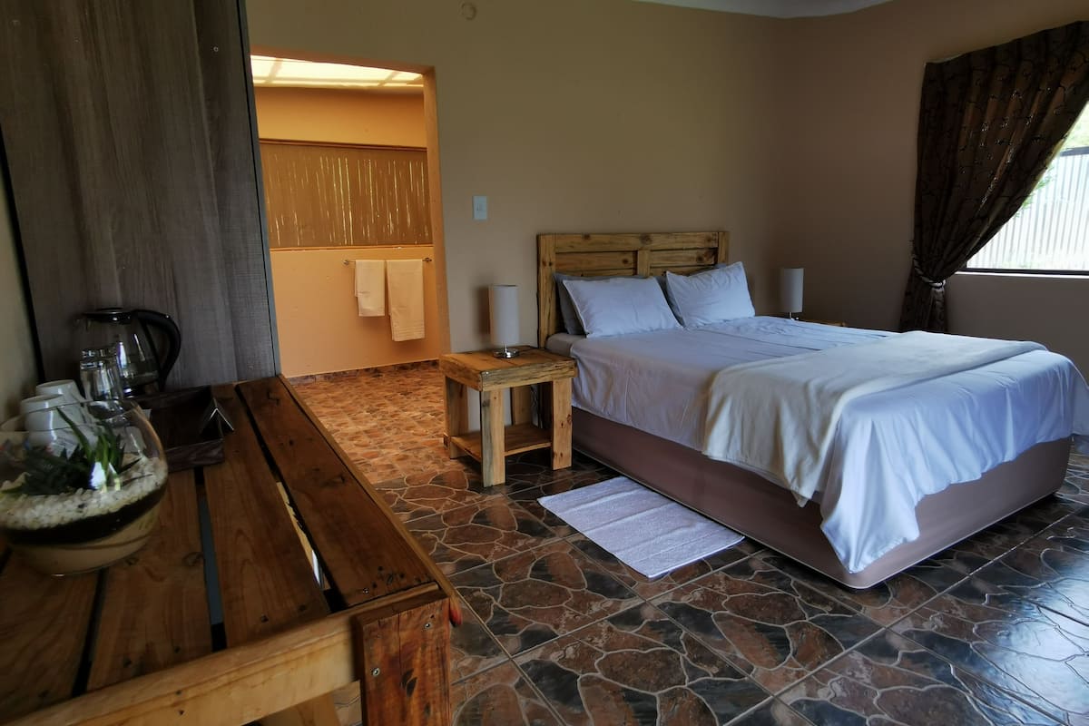 A bedroom with a bed, wooden nightstand, and a table with a glass container.