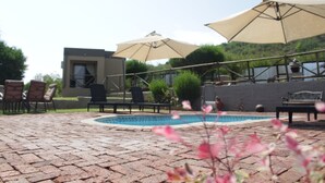 Un patio de ladrillo con piscina, mobiliario exterior y sombrillas.