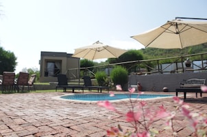 Um terraço de tijolos com piscina, móveis de exterior e guarda-sóis.