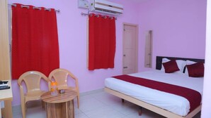 A bedroom with a bed, two chairs, a small table, a door, and an air conditioning unit. - GP Residency (Gingee)