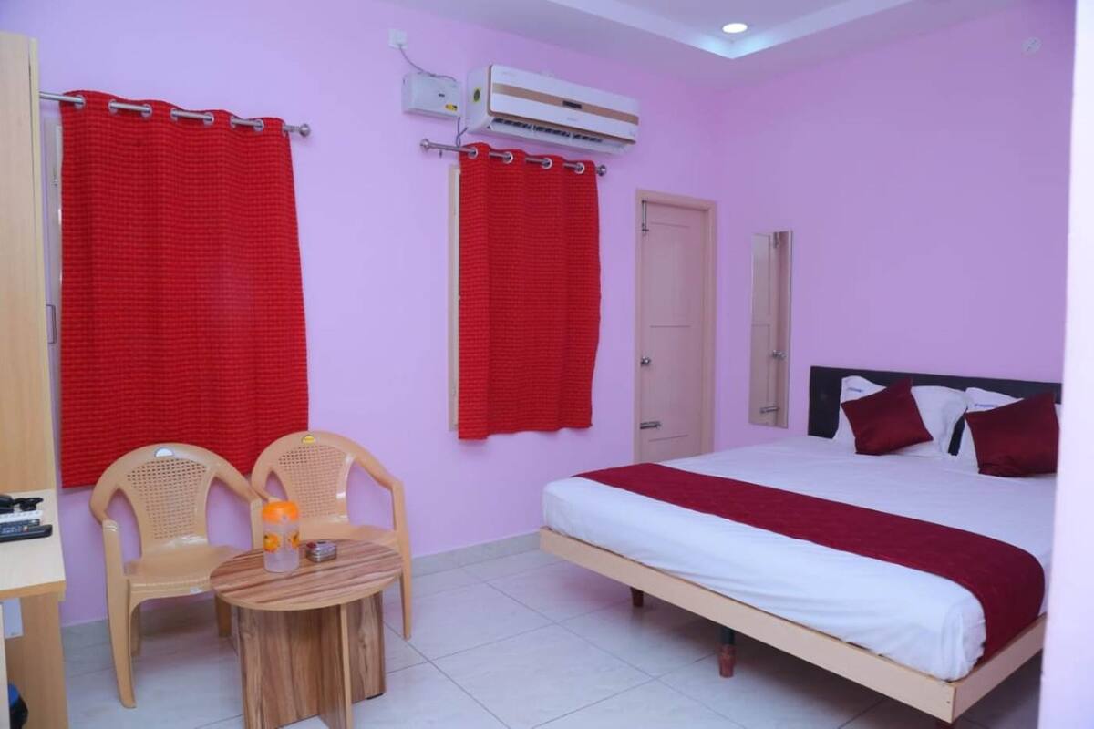 A bedroom with a bed, two chairs, a small table, an air conditioning unit, and a door.