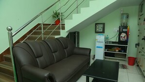 A living room with a brown leather sofa, a black coffee table, a staircase, a water dispenser, and a framed picture on the wall. - GP Residency (Gingee)