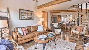 A spacious living room with a brown leather sofa, a wooden coffee table, and a staircase with a spiral design. - Private Balcony & Resort Perks: Silverthorne Condo (Silverthorne)