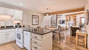 A modern kitchen with white cabinets, a central island, and a dining area with a wooden table and chairs. - Private Balcony & Resort Perks: Silverthorne Condo (Silverthorne)
