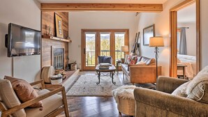 A cozy living room with a fireplace, wooden beams, a television, and a sofa. - Private Balcony & Resort Perks: Silverthorne Condo (Silverthorne)