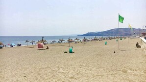A beach with umbrellas, a flag, and a distant mountain.