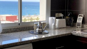 A kitchen with a washing machine, a coffee maker, and a view of the ocean.