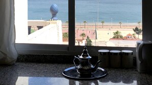 A kitchen with a view of the sea through a window, a teapot on the counter, and three stainless steel containers.