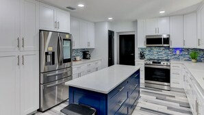 Una cocina moderna con armarios blancos, electrodomésticos de acero inoxidable, una isla azul y un salpicadero con diseño.