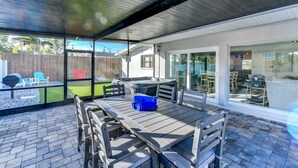Un patio al aire libre con una mesa, sillas, una parrilla y vista al jardín trasero.