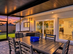 An outdoor patio area with a table and chairs, a hot tub, and a glass door leading to an indoor space.