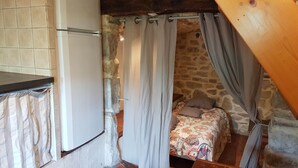 A small, rustic room with a bed, a white refrigerator, and a stone wall. - Village house and garden, breathtaking view (Saint-Sauveur-de-Cruzières)