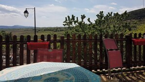 A terrace with a wooden fence, a table with a patterned tablecloth, and a view of a vineyard and hills. - Village house and garden, breathtaking view (Saint-Sauveur-de-Cruzières)