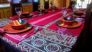 Una mesa de comedor dispuesta con platos, cuencos y cubiertos rojos y negros, cubierta por un mantel estampado.