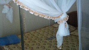 A bed with a mosquito net and patterned bedding. - Pivot Hotel (Mwingi)
