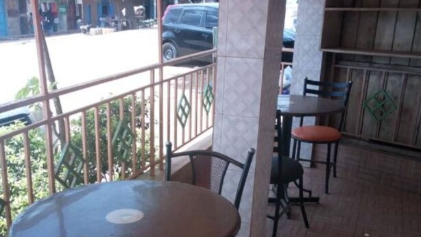 An outdoor seating area with a round table and chairs, a tiled floor, and a view of the street. - Pivot Hotel (Mwingi)