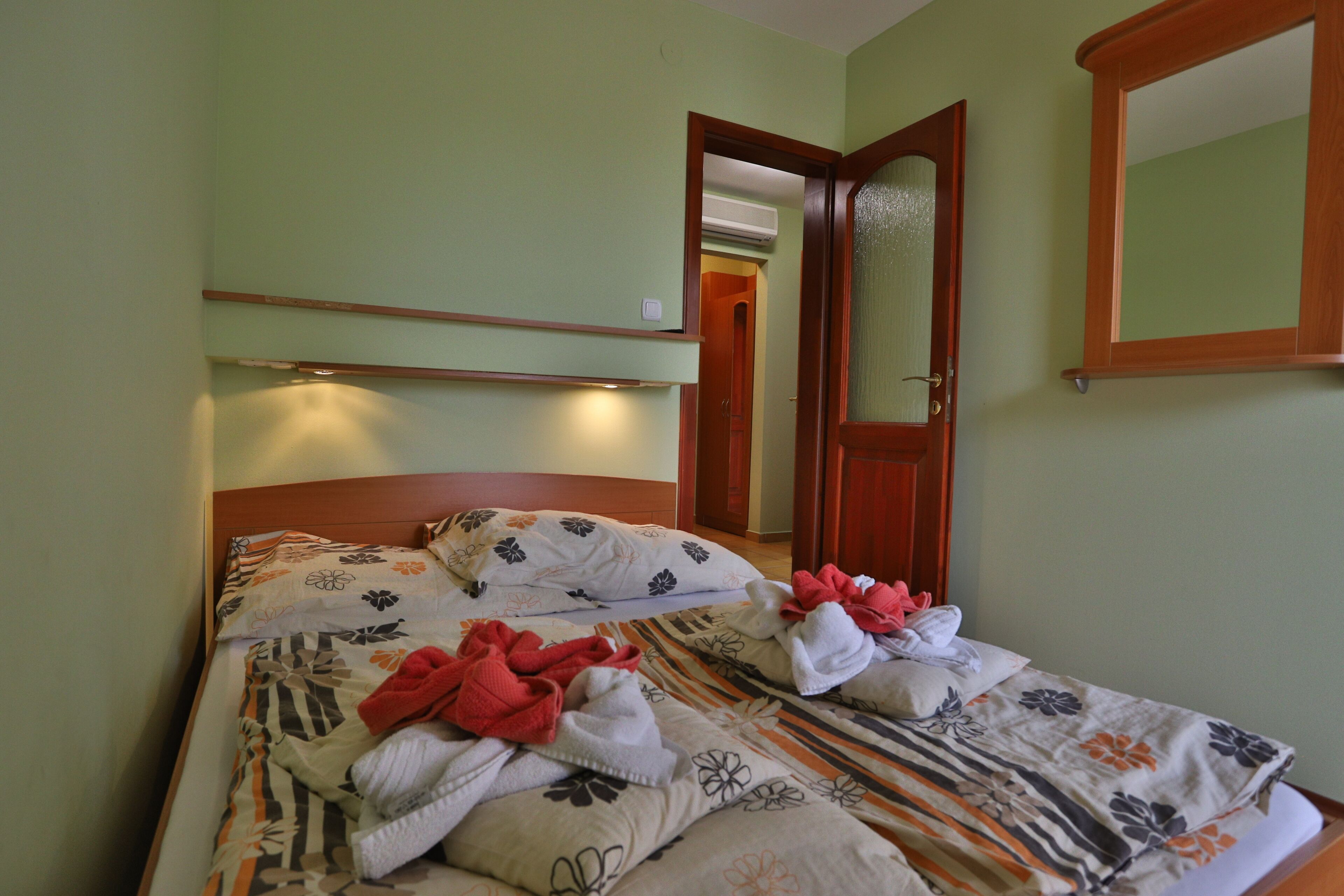Habitación de hotel con cama, cabecera de madera, espejo y puerta.