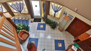 A hotel lobby with a staircase, a reception desk, and potted plants.