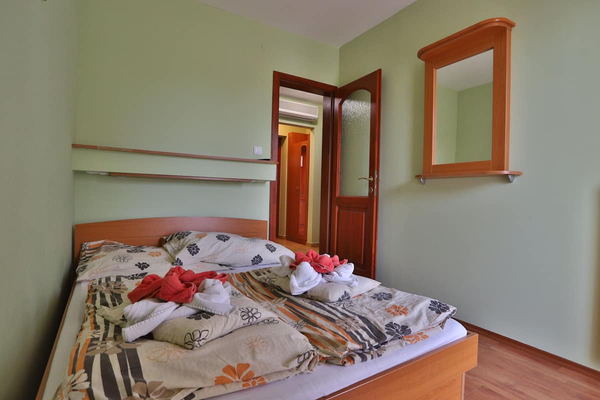 A neatly made bed with floral bedding, a wooden headboard, and a mirror on the wall.