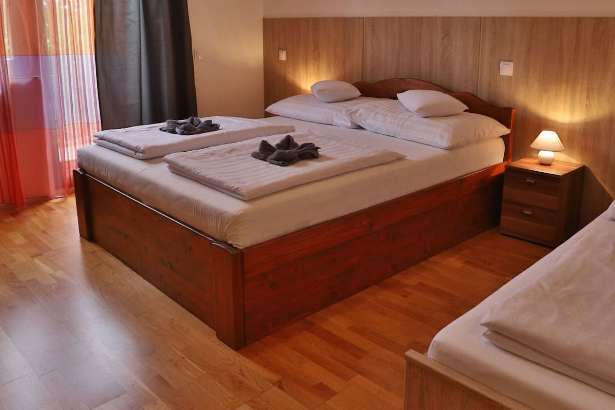 A hotel room with a wooden bed, a bedside table with a lamp, and a window with curtains.