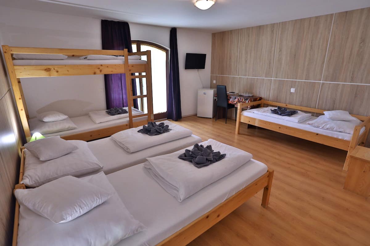 A room with two bunk beds, a desk, a chair, and a television on the wall.