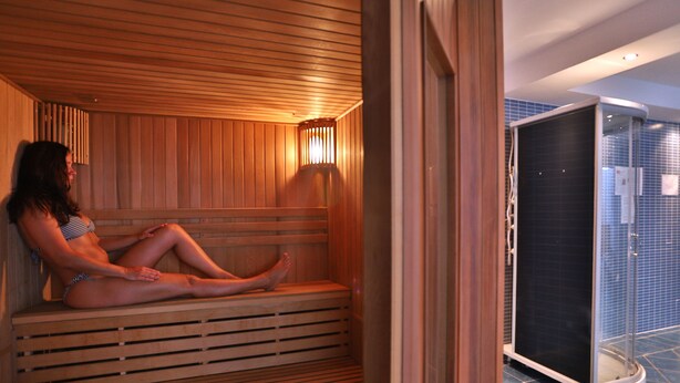 A sauna with wooden benches and a glass door leading to a bathroom.