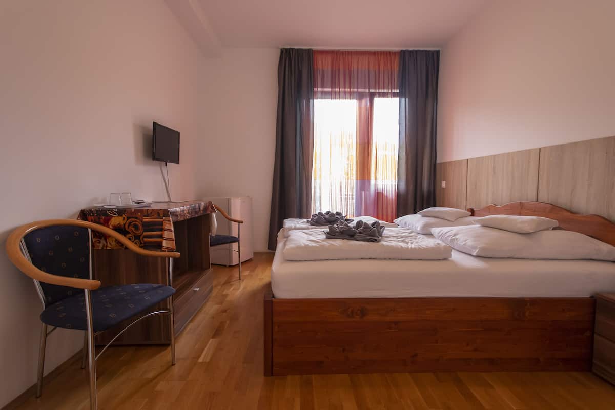 A hotel room with a wooden bed, a desk with a chair, a television, and a window with curtains.