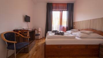 Une chambre d’hôtel avec un lit en bois, un bureau avec une chaise, une télévision et une fenêtre avec des rideaux.