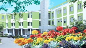 Un hotel de varios pisos con fachada verde y blanca, un letrero vertical llamativo y un colorido jardín de flores en primer plano.