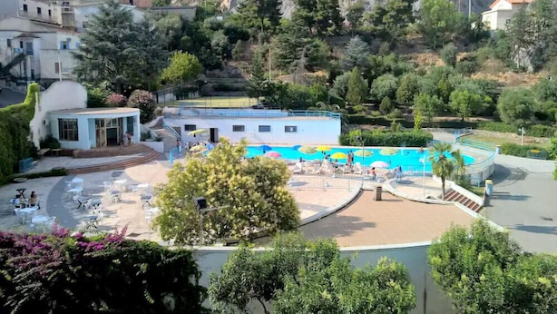 Un resort con piscina, mobiliario exterior y montañas al fondo.