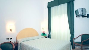 Una habitación de hotel con cama, una silla, un escritorio y un televisor montado en la pared.