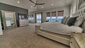 A spacious bedroom with a large bed, a ceiling fan, and a view of the ocean. - The Hidden Gem ~Luxurious Beachfront Home Near 30A! (Panama City Beach)