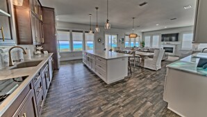 A spacious kitchen with a large island, dark wood flooring, and a view of the ocean. - The Hidden Gem ~Luxurious Beachfront Home Near 30A! (Panama City Beach)