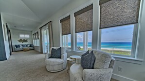 A spacious living room with a view of the ocean, large windows with blinds, a sofa, and two armchairs. - The Hidden Gem ~Luxurious Beachfront Home Near 30A! (Panama City Beach)